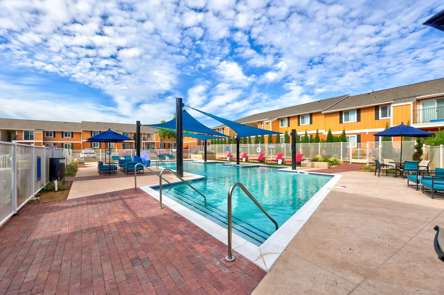 A pool surrounded by a brick patio and umbrellas.